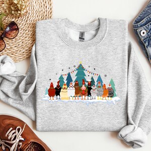 May include: A gray sweatshirt with a Christmas-themed design featuring a group of chickens wearing festive hats and scarves in front of a snowy forest scene. The text "Merry Christmas" is printed on the sweatshirt.