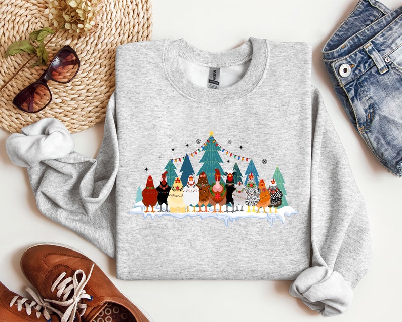 May include: A gray sweatshirt with a Christmas-themed design featuring a group of chickens wearing festive hats and scarves in front of a snowy forest scene. The text "Merry Christmas" is printed on the sweatshirt.