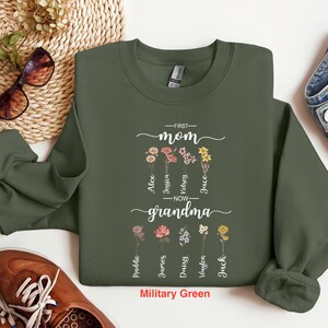May include: A military green sweatshirt with the text "First Mom Now Grandma" and floral designs. The text is surrounded by names, including Alex, Jessica, Kelsey, Grace,  and more.