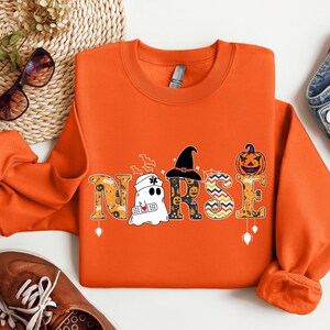 May include: Orange sweatshirt with a Halloween-themed "NURSE" graphic. The letters are decorated with ghosts, pumpkins, and witch hats.