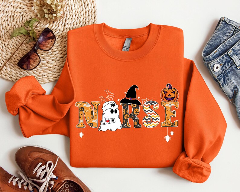 May include: Orange sweatshirt with a Halloween-themed "NURSE" graphic. The letters are decorated with ghosts, pumpkins, and witch hats.