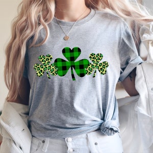 May include: A gray t-shirt with a design of three shamrocks. The shamrocks are green and black plaid, and yellow and green leopard print.