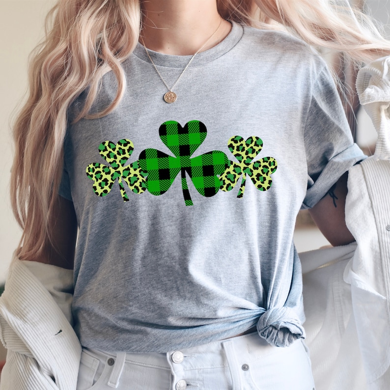 May include: A gray t-shirt with a design of three shamrocks. The shamrocks are green and black plaid, and yellow and green leopard print.