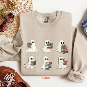 Może przedstawiać: Beżowa bluza z nadrukiem sześciu duch&oacute;w trzymających stosy książek. Na dole bluzy znajduje się napis "SAND".