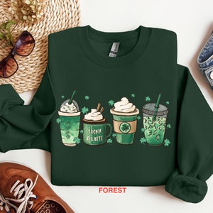 May include: Green sweatshirt with a graphic of four different coffee drinks with shamrocks and the text "Lucky a Latte".