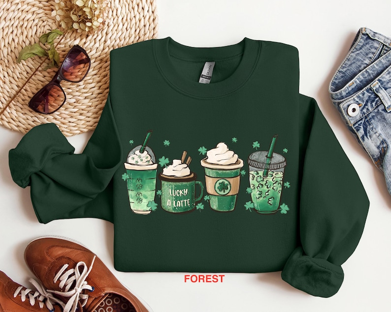 May include: Green sweatshirt with a graphic of four different coffee drinks with shamrocks and the text "Lucky a Latte".