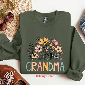 Puede incluir: Una sudadera verde con un dise&ntilde;o floral y la palabra "Grandma" en letras de colores. La sudadera est&aacute; sobre un fondo blanco.