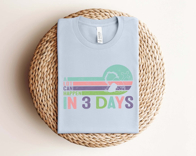 Puede incluir: Camiseta azul claro con un gr&aacute;fico de estilo retro que dice "A lot can happen in 3 days". El gr&aacute;fico presenta un dise&ntilde;o a rayas de colores con una ola y una palmera.