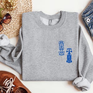 Peut inclure: Un sweat-shirt gris avec un motif bleu de deux voitures de course sur le devant.
