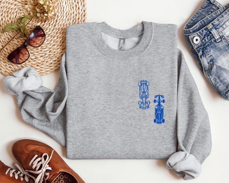 Peut inclure: Un sweat-shirt gris avec un motif bleu de deux voitures de course sur le devant.