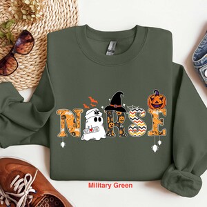 May include: A military green sweatshirt with a Halloween-themed design featuring the word "NURSE" with a ghost, witch hat, and pumpkin.
