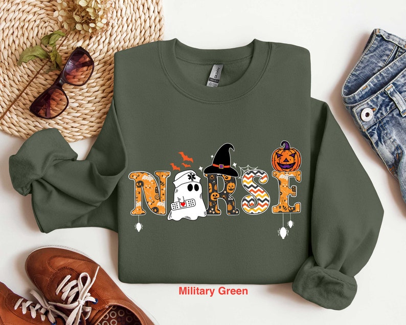 May include: A military green sweatshirt with a Halloween-themed design featuring the word "NURSE" with a ghost, witch hat, and pumpkin.