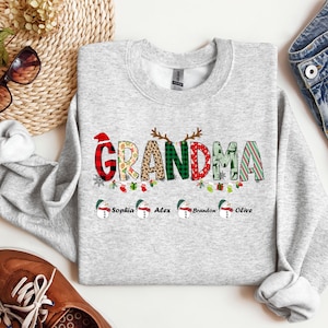 May include: A gray Christmas sweatshirt with the word "Grandma" in colorful letters with a festive design. The names "Sophia", "Alex", "Brandon", and "Olive" are printed below the word "Grandma".