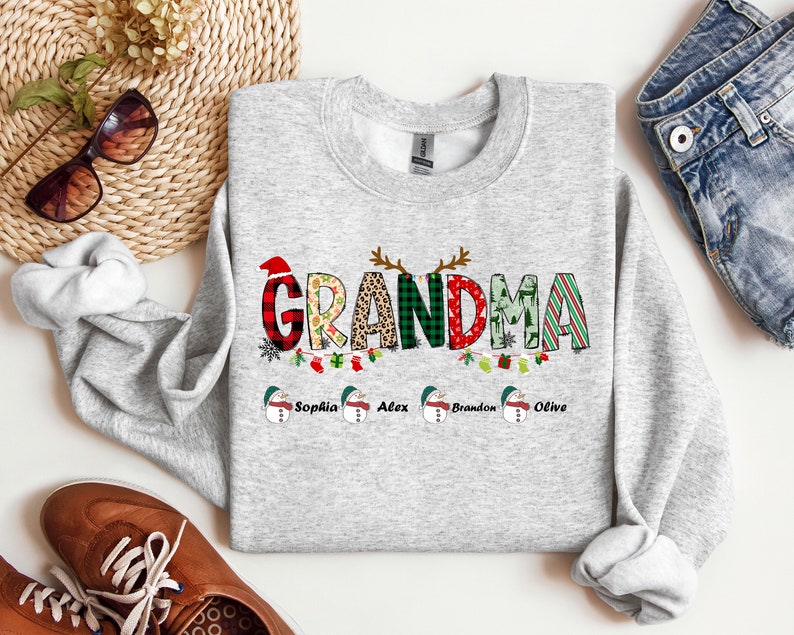 May include: A gray Christmas sweatshirt with the word "Grandma" in colorful letters with a festive design. The names "Sophia", "Alex", "Brandon", and "Olive" are printed below the word "Grandma".
