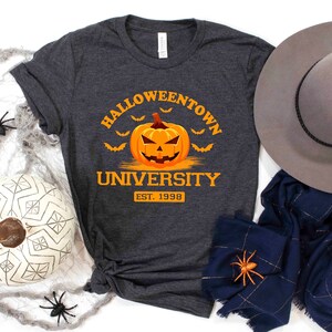May include: A dark gray t-shirt with the text "Halloweentown University Est. 1998" and a cartoon orange pumpkin with a jack-o-lantern face.