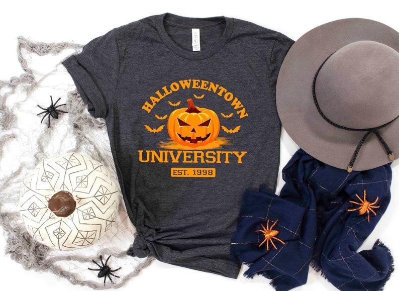 May include: A dark gray t-shirt with the text "Halloweentown University Est. 1998" and a cartoon orange pumpkin with a jack-o-lantern face.