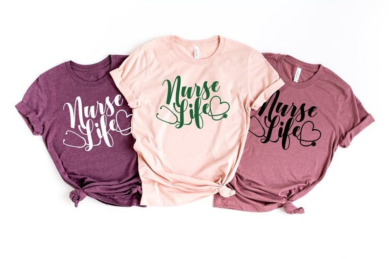 K&ouml;nnte beinhalten: Drei T-Shirts mit dem Text "Nurse Life" in einer kursiven Schrift. Die Shirts sind in verschiedenen Farben: weinrot, rosa und hellrosa. Jedes Shirt hat ein Stethoskop und ein Herz-Motiv.