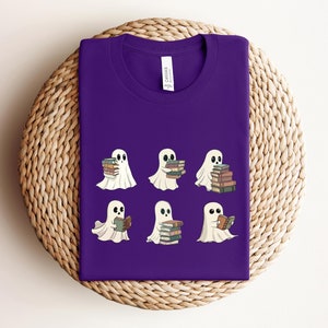 Może przedstawiać: Fioletowy T-shirt z wzorem sześciu białych duch&oacute;w trzymających lub czytających książki. Duchy mają czarne oczy i są w r&oacute;żnych pozach.