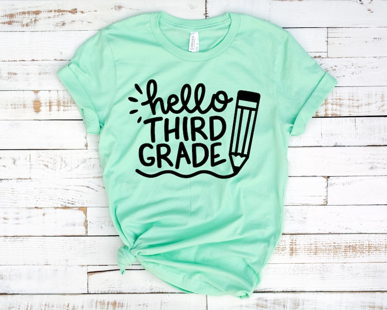 Op de afbeelding: Een lichtgroen T-shirt met de tekst "hello third grade" en een zwarte potloodtekening.