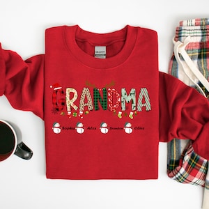 May include: Red Christmas sweatshirt with the word "Grandma" in colorful patterned letters.  The letters are decorated with snowflakes, ornaments, and holly.  Below the word "Grandma" are five snowmen with the names "Sophia", "Alex", "Brandon", and "Olive" written below them.