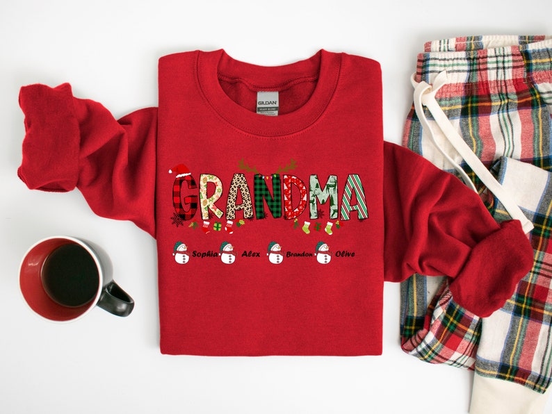 May include: Red Christmas sweatshirt with the word "Grandma" in colorful patterned letters.  The letters are decorated with snowflakes, ornaments, and holly.  Below the word "Grandma" are five snowmen with the names "Sophia", "Alex", "Brandon", and "Olive" written below them.