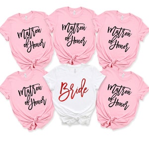 May include: Five pink t-shirts with black text that says "Matron of Honor" and one white t-shirt with red glitter text that says "Bride".