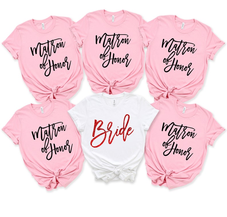 May include: Five pink t-shirts with black text that says "Matron of Honor" and one white t-shirt with red glitter text that says "Bride".