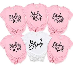 May include: Five t-shirts, four pink and one white, with the words "Bride" and "Bridesmaid" written in black script.