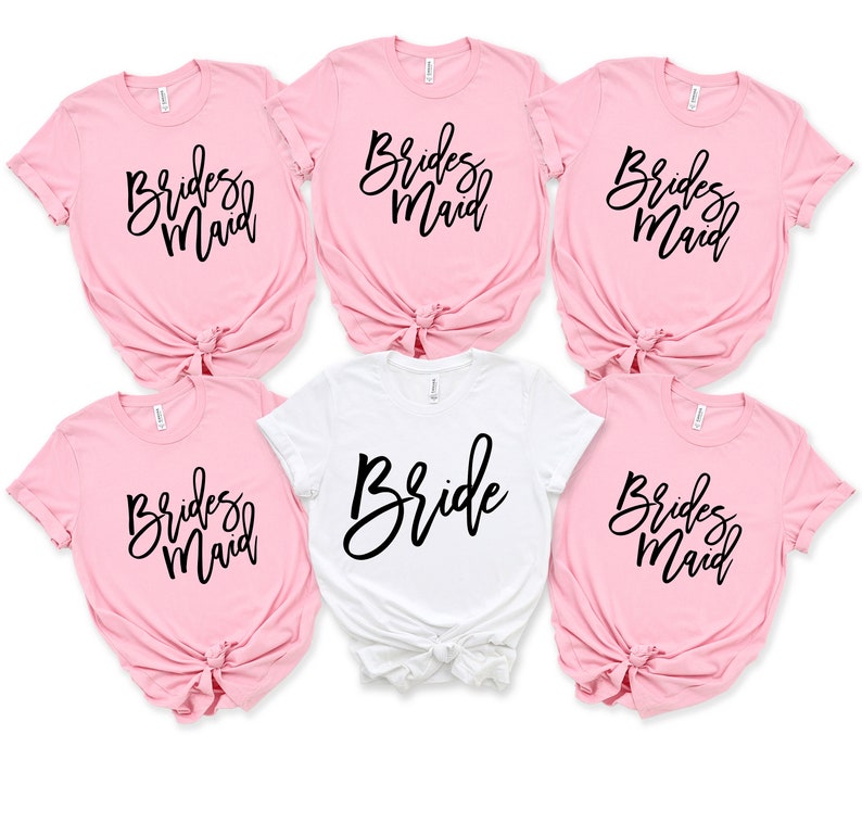 May include: Five t-shirts, four pink and one white, with the words "Bride" and "Bridesmaid" written in black script.