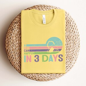 Puede incluir: Una camiseta amarilla con un gr&aacute;fico de estilo retro que dice "Muchas cosas pueden pasar en 3 d&iacute;as". El gr&aacute;fico presenta un fondo a rayas de colores y una silueta de una persona con una corona de espinas.