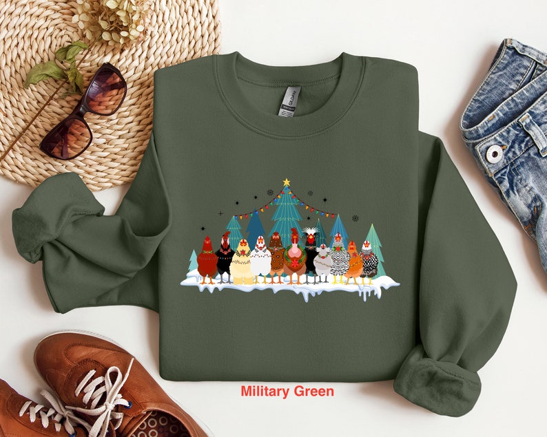 May include: A military green sweatshirt with a Christmas-themed design featuring a group of chickens in front of a decorated Christmas tree. The text "Military Green" is printed on the bottom of the sweatshirt.