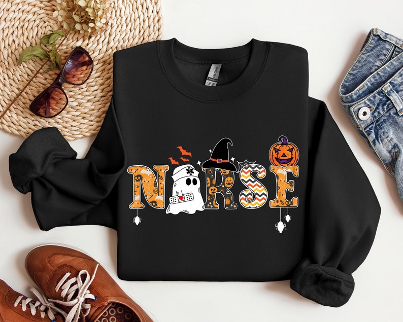 May include: Black sweatshirt with a Halloween-themed "NURSE" graphic. The graphic features a ghost, a witch's hat, a pumpkin, and other Halloween elements.