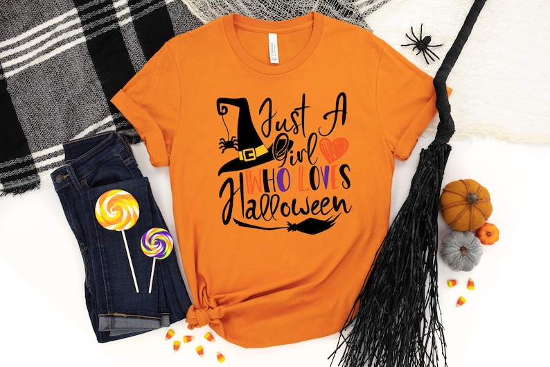 May include: Orange t-shirt with a black witch hat, spider, and broom graphic. The text on the shirt reads "Just a girl who loves Halloween".