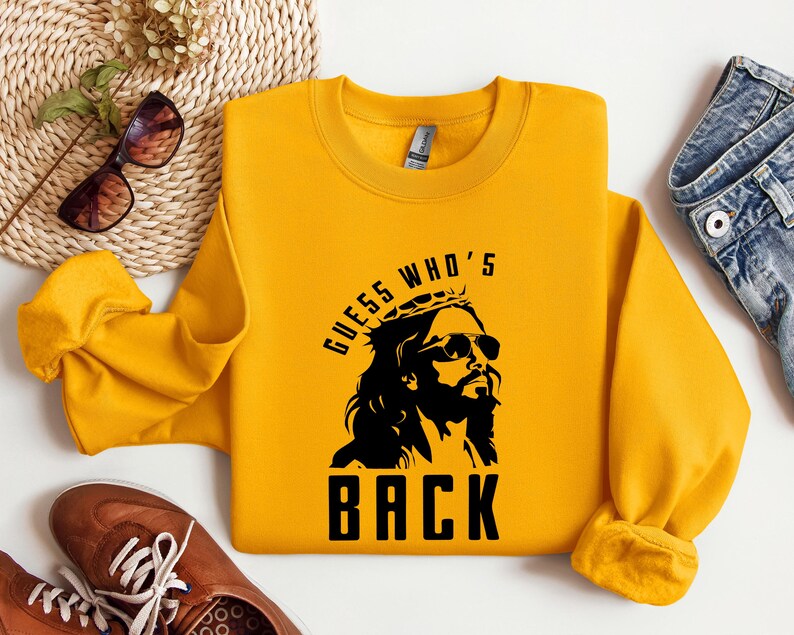 Puede incluir: Sudadera amarilla con un gr&aacute;fico negro de Jes&uacute;s con gafas de sol y una corona de espinas. El texto "Guess Who's Back" est&aacute; impreso debajo del gr&aacute;fico.