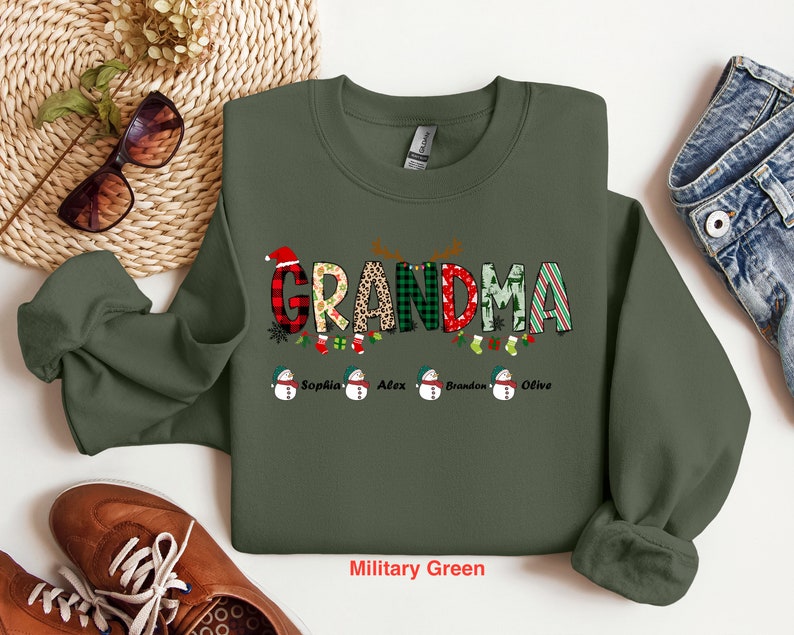 May include: A green Christmas sweatshirt with the word "Grandma" in colorful letters and a snowman design. The names "Sophia", "Alex", "Brandon", and "Olive" are printed below the snowman design.