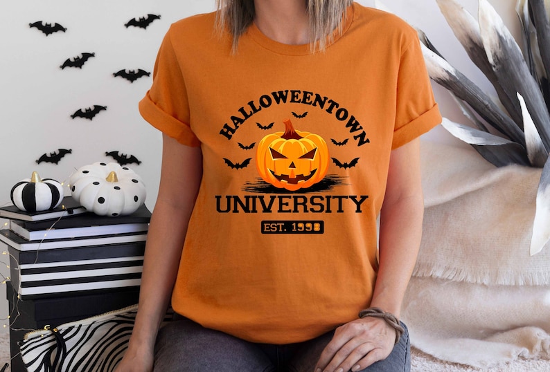 May include: Orange t-shirt with a black graphic of a jack-o'-lantern with the text "Halloweentown University Est. 1998"