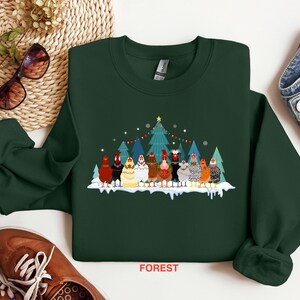 May include: A dark green sweatshirt with a Christmas-themed design featuring a group of chickens standing in front of a decorated Christmas tree. The text "FOREST" is printed on the bottom of the sweatshirt.