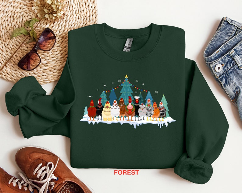 May include: A dark green sweatshirt with a Christmas-themed design featuring a group of chickens standing in front of a decorated Christmas tree. The text "FOREST" is printed on the bottom of the sweatshirt.