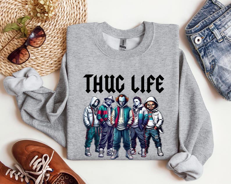 Peut inclure: Un sweat-shirt gris chin&eacute; avec l'inscription "THUG LIFE" en noir, dans une police gothique. Le sweat-shirt pr&eacute;sente un graphisme de cinq personnages de dessins anim&eacute;s portant des sweats &agrave; capuche et des vestes. Les personnages sont dans des tons de bleu, de rouge, de vert et de blanc.