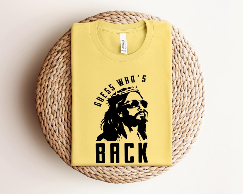 Puede incluir: Camiseta amarilla con un gr&aacute;fico negro de una persona con una corona de espinas y gafas de sol. El texto "Guess Who's Back" est&aacute; impreso debajo del gr&aacute;fico.