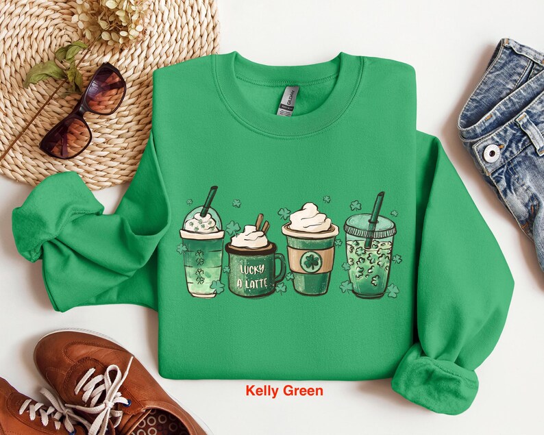 May include: Green sweatshirt with a graphic of four different green drinks with shamrock designs. The text "Lucky a Latte" is on one of the drinks. The sweatshirt is labeled "Kelly Green".