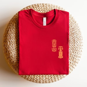Peut inclure: T-shirt rouge avec un contour jaune de deux voitures de course sur le devant.