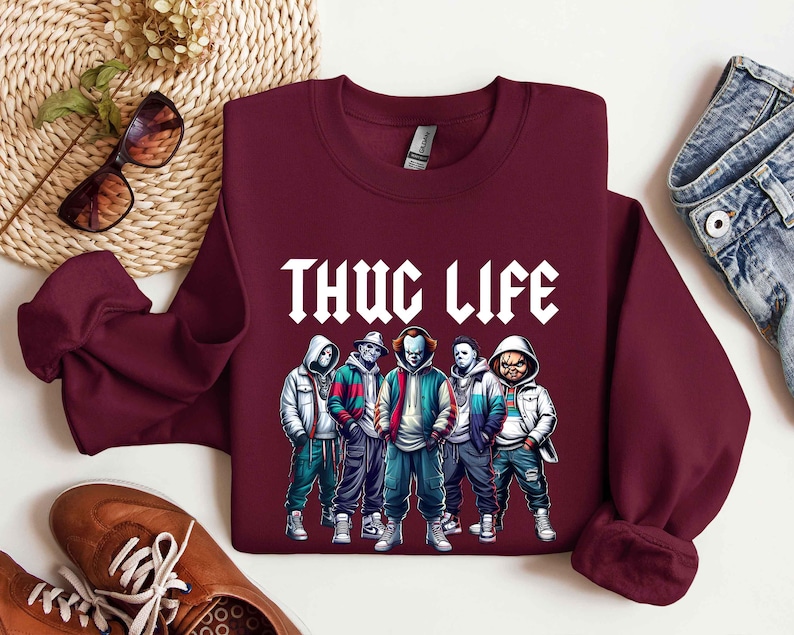 Peut inclure: Un sweat-shirt bordeaux avec le texte blanc "THUG LIFE" et un graphisme de cinq personnages de dessins anim&eacute;s en vestes et sweats &agrave; capuche. Les personnages ont un th&egrave;me d'horreur.