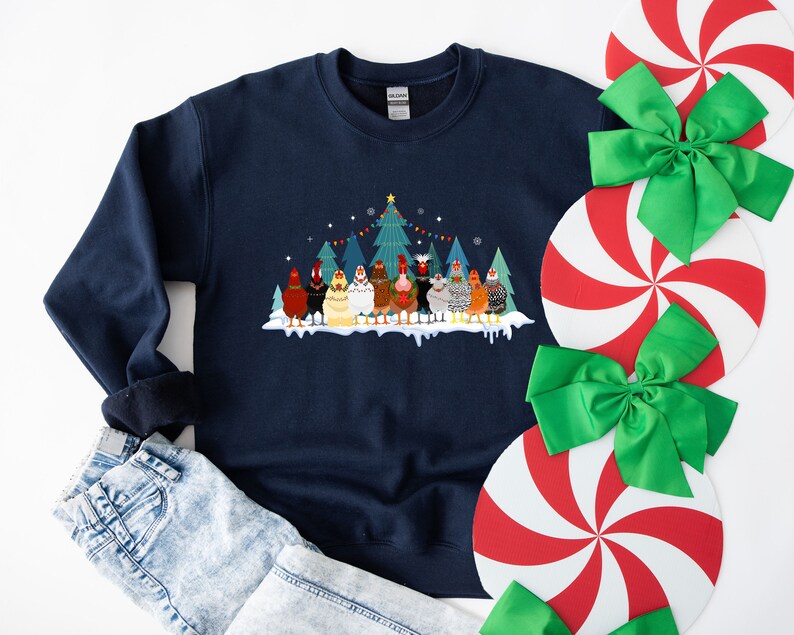 May include: A navy blue sweatshirt with a Christmas-themed design featuring a group of chickens standing in front of a decorated Christmas tree. The chickens are wearing festive hats and scarves.