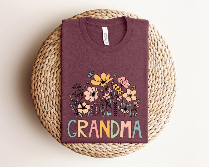Puede incluir: Una camiseta color granate con un dise&ntilde;o floral y la palabra "GRANDMA" en letras de colores.