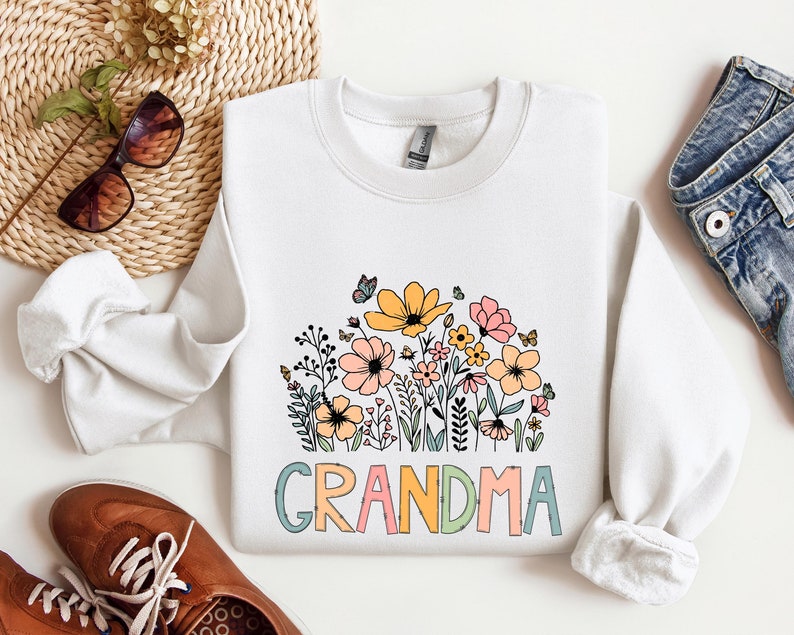 Puede incluir: Sudadera blanca con un dise&ntilde;o floral y la palabra "Abuela" en letras de colores.