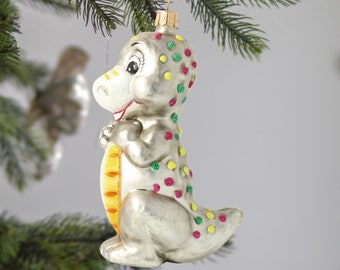 May include: A silver glass Christmas ornament shaped like a dinosaur with green, yellow, and pink polka dots.