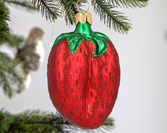 May include: A red glass Christmas bauble shaped like a strawberry with green leaves. The bauble has a glittery finish.