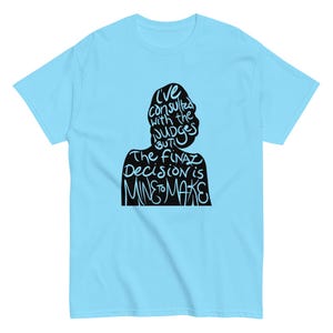May include: Light blue t-shirt with a black silhouette of a person's head and shoulders. The silhouette contains the text "I've consulted with the judges but the final decision is mine to make" in white.