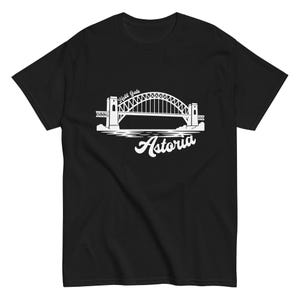 May include: A black short-sleeved t-shirt featuring a white graphic print of the Hell Gate Bridge. The design includes the text "Hell Gate" arched above the bridge and the word "Astoria" in a stylized script font positioned below the bridge illustration.